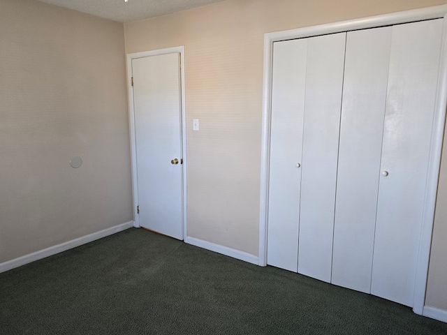 unfurnished bedroom featuring dark colored carpet, a closet, and baseboards