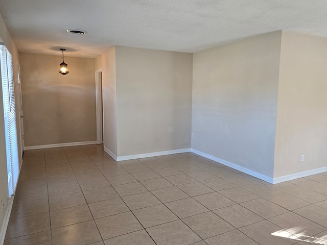 empty room with a textured ceiling, light tile patterned floors, visible vents, and baseboards