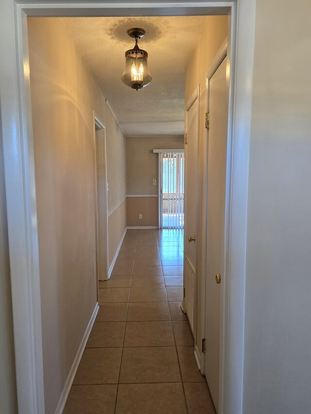 hallway with tile patterned flooring, baseboards, and a textured ceiling