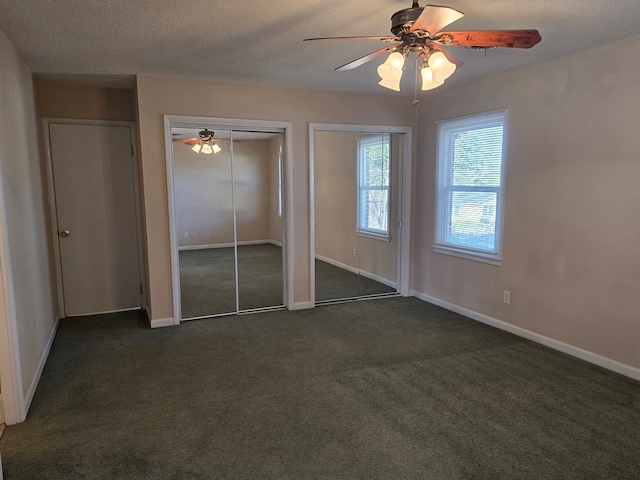 unfurnished bedroom with baseboards, ceiling fan, dark colored carpet, a textured ceiling, and two closets