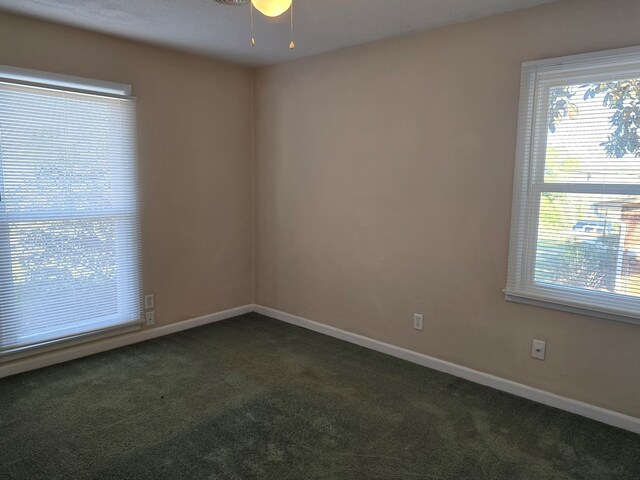 unfurnished room with dark carpet, plenty of natural light, and baseboards