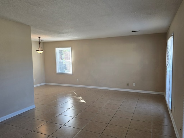 unfurnished room with light tile patterned floors, a textured ceiling, and baseboards