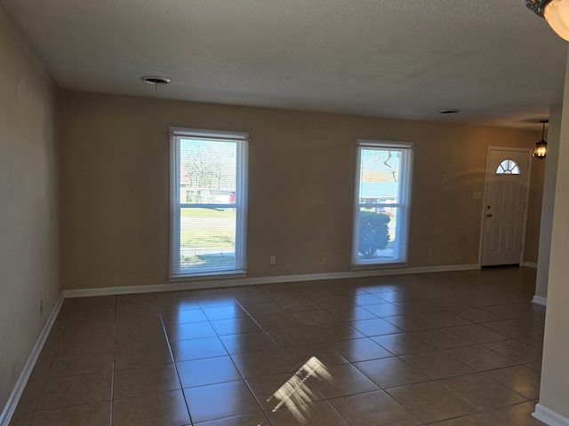 tiled empty room featuring baseboards, plenty of natural light, visible vents, and a textured ceiling