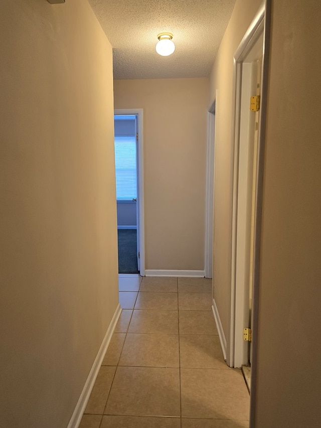 hallway featuring light tile patterned floors, baseboards, and a textured ceiling