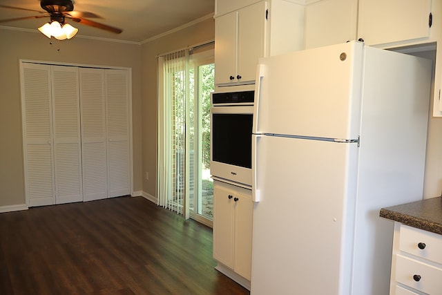 kitchen featuring dark wood-type flooring, oven, crown molding, white fridge, and white cabinetry