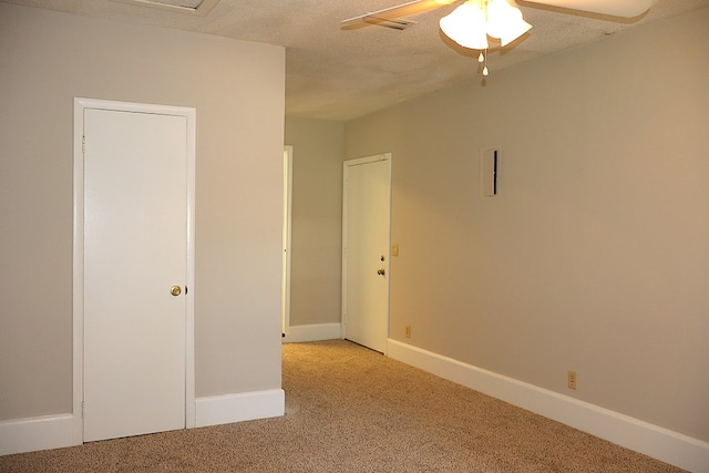 empty room with ceiling fan, light colored carpet, and a textured ceiling