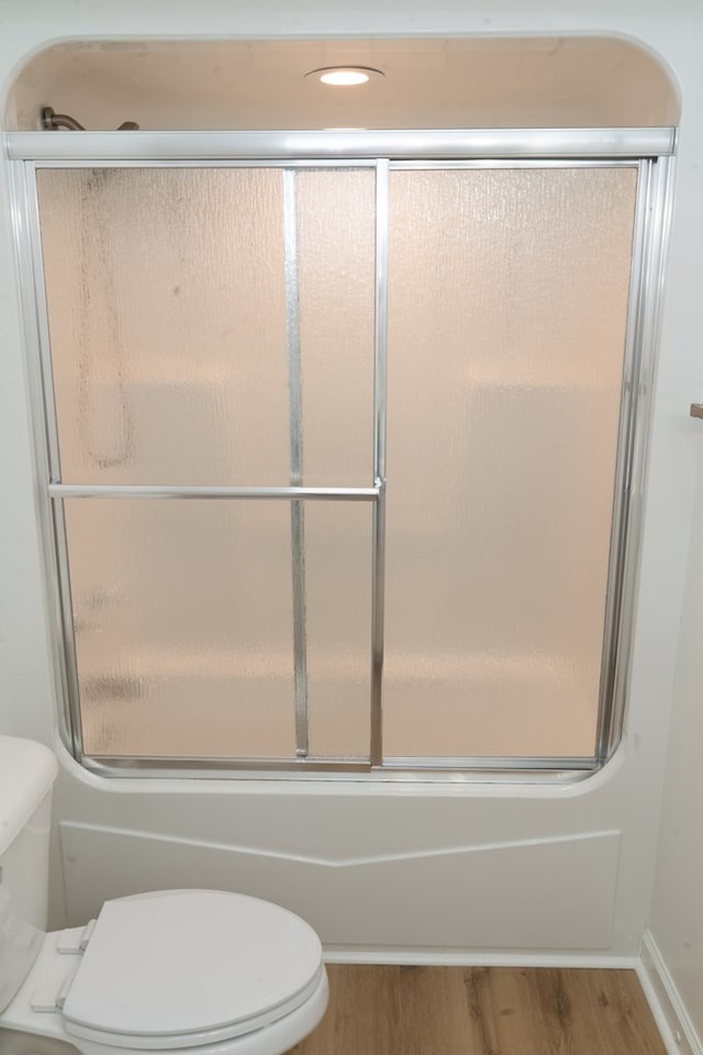 bathroom featuring toilet, bath / shower combo with glass door, and hardwood / wood-style floors