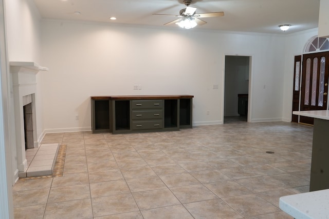 unfurnished living room featuring ceiling fan, ornamental molding, a tile fireplace, and light tile patterned floors