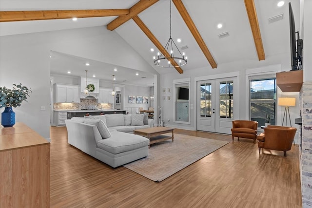 living room with french doors, high vaulted ceiling, beamed ceiling, a notable chandelier, and light hardwood / wood-style floors