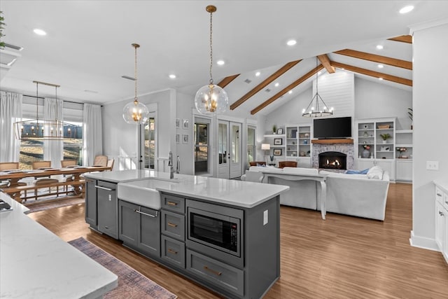 kitchen featuring stainless steel microwave, a kitchen island with sink, gray cabinets, beamed ceiling, and decorative light fixtures