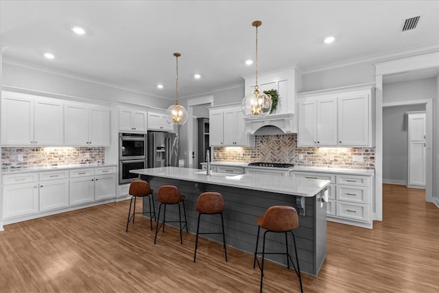 kitchen featuring a breakfast bar area, white cabinets, an island with sink, and appliances with stainless steel finishes