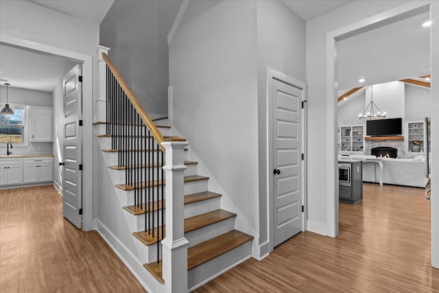 stairs with a stone fireplace, sink, wood-type flooring, and vaulted ceiling