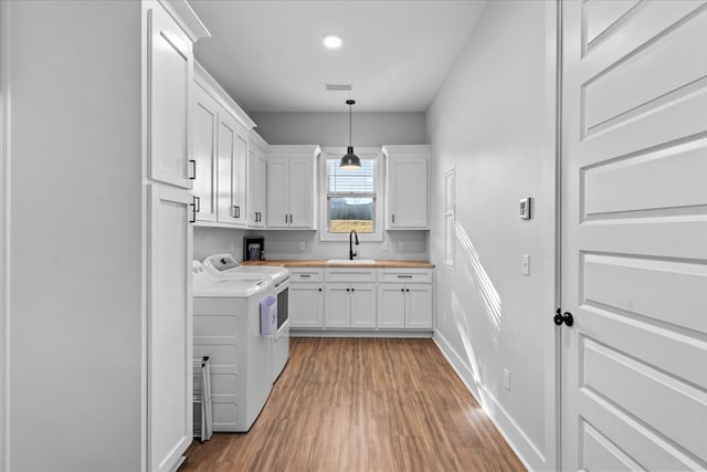 kitchen featuring pendant lighting, hardwood / wood-style floors, sink, washing machine and dryer, and white cabinetry