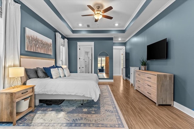 bedroom with hardwood / wood-style floors, a raised ceiling, ceiling fan, and crown molding