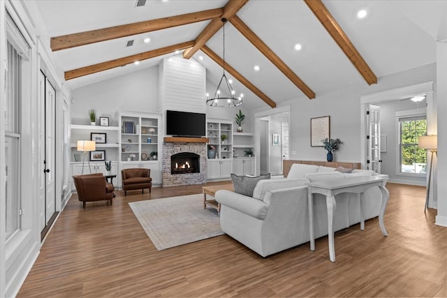 living room with a stone fireplace, built in shelves, high vaulted ceiling, and hardwood / wood-style flooring