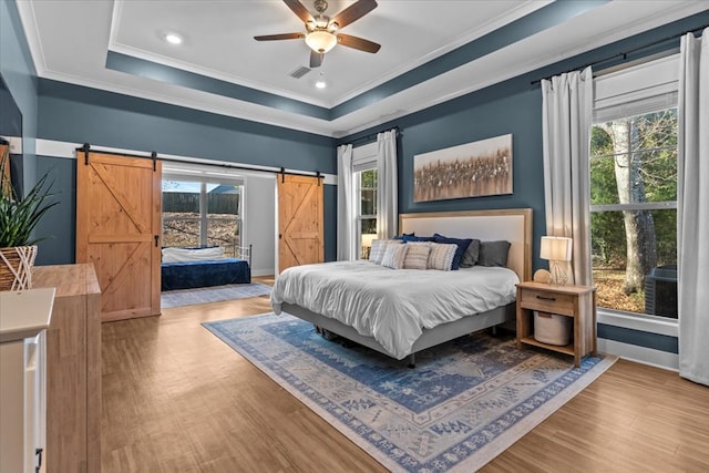 bedroom featuring a barn door, ceiling fan, light hardwood / wood-style flooring, and multiple windows