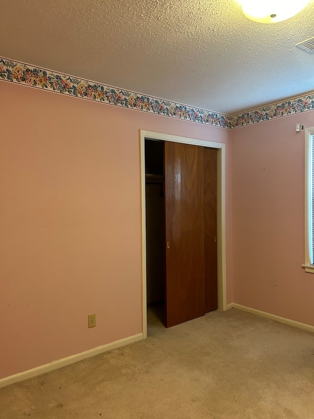 unfurnished bedroom featuring a textured ceiling, light colored carpet, and a closet