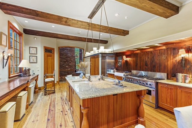 kitchen featuring a kitchen island with sink, light hardwood / wood-style flooring, high end range, and hanging light fixtures