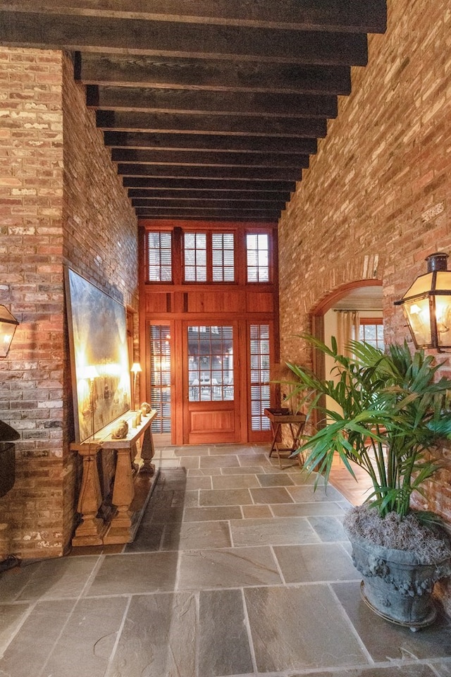 hall featuring beamed ceiling, a towering ceiling, and brick wall