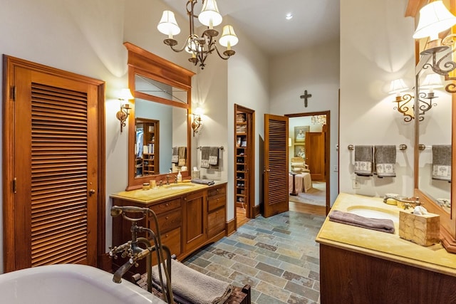 bathroom with a notable chandelier, vanity, a towering ceiling, and a bath