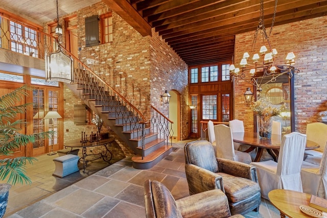 unfurnished dining area featuring a high ceiling, beamed ceiling, wood ceiling, brick wall, and a chandelier