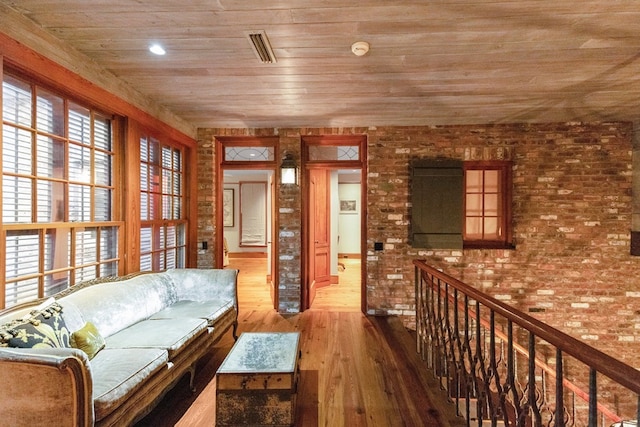 sitting room featuring wood-type flooring, wooden ceiling, and brick wall