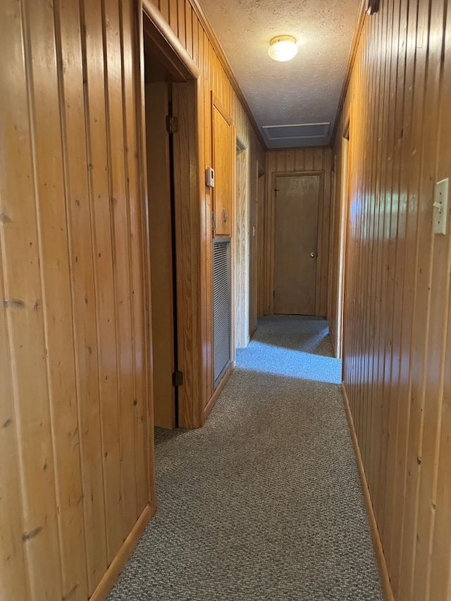 hallway with wood walls, carpet floors, and a textured ceiling