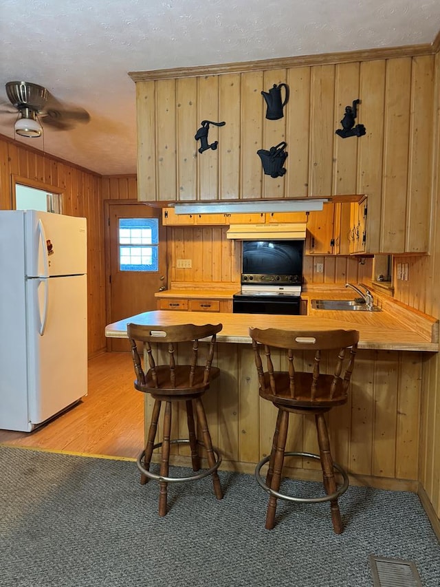 kitchen with kitchen peninsula, a kitchen bar, light wood-type flooring, sink, and white refrigerator