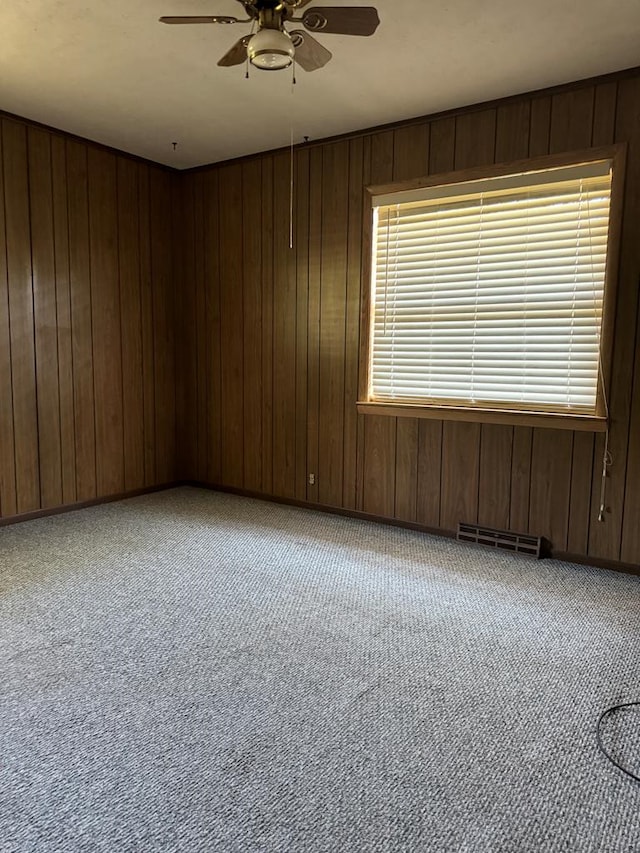 spare room featuring light carpet, ceiling fan, and wood walls