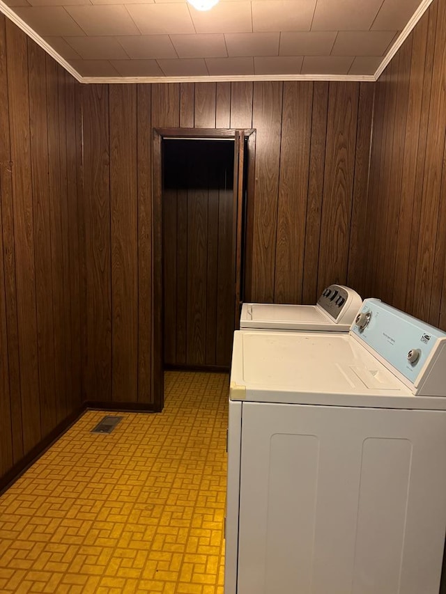 clothes washing area with washer and dryer, crown molding, and wooden walls