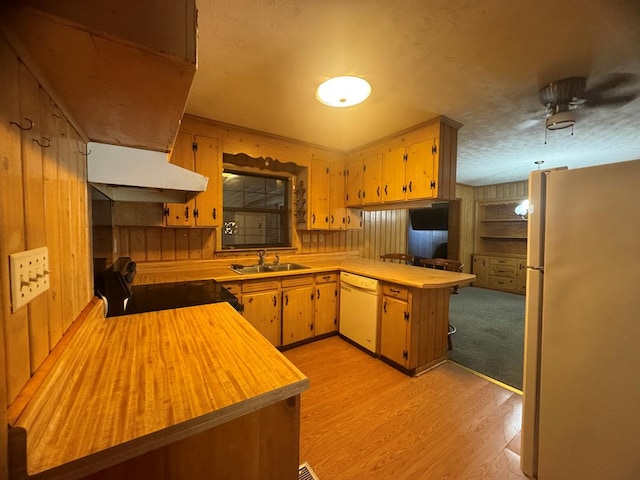 kitchen featuring kitchen peninsula, white appliances, sink, light hardwood / wood-style flooring, and wood walls