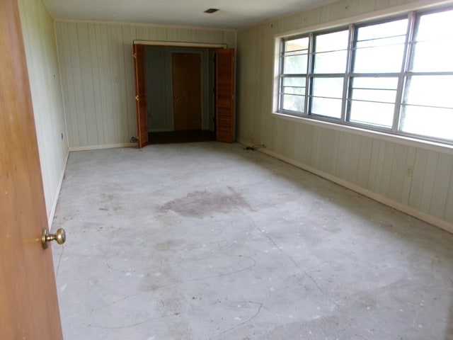 spare room featuring wood walls, unfinished concrete flooring, and baseboards