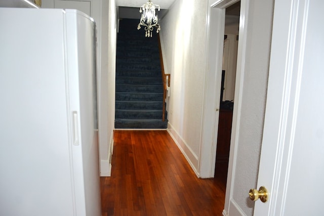 corridor featuring dark wood-type flooring, baseboards, stairway, and a notable chandelier
