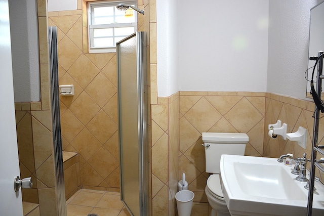 full bathroom with a wainscoted wall, toilet, a sink, tile walls, and a stall shower