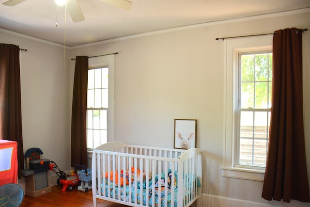 bedroom featuring wood finished floors, ornamental molding, multiple windows, and a nursery area