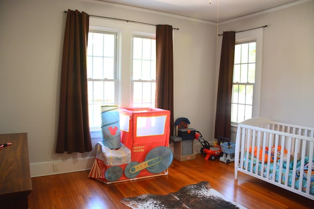 bedroom featuring baseboards, multiple windows, ornamental molding, and wood finished floors