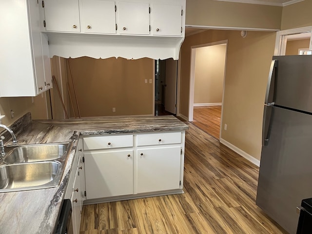 kitchen with stainless steel fridge, sink, white cabinets, and wood-type flooring