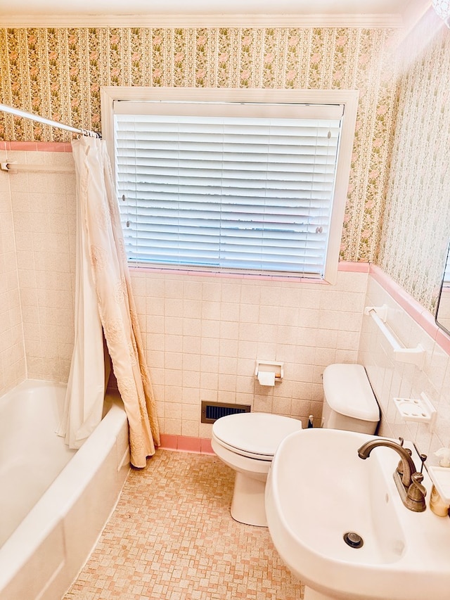full bath featuring tile walls, a sink, toilet, shower / bath combo with shower curtain, and wallpapered walls