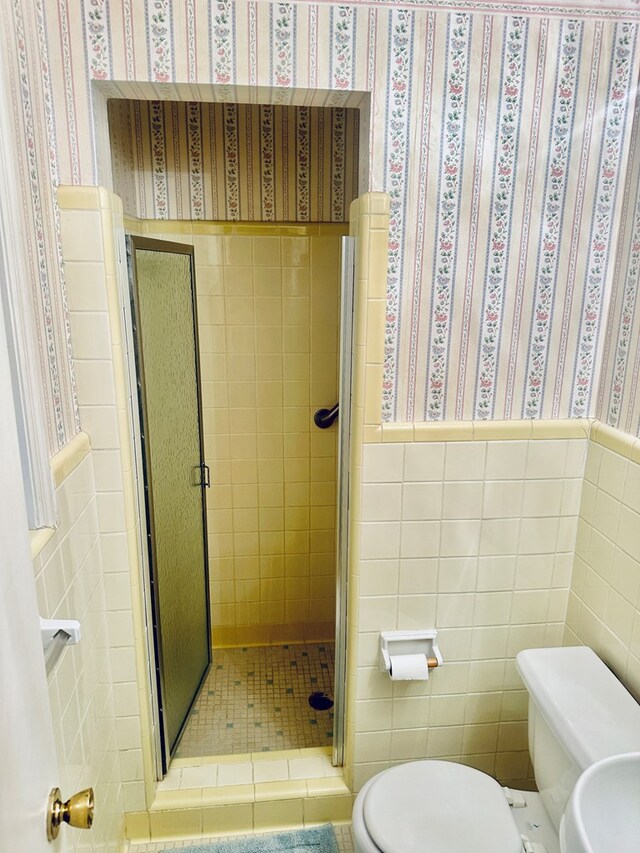 bathroom featuring tile walls, wainscoting, a shower stall, toilet, and wallpapered walls