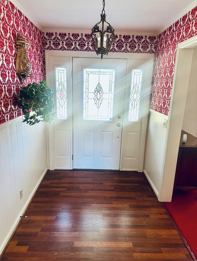 entrance foyer with dark wood-style flooring, wallpapered walls, ornamental molding, and a wainscoted wall