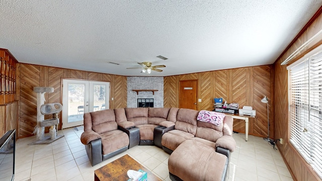 living room featuring a textured ceiling, ceiling fan, light tile patterned floors, a fireplace, and wood walls