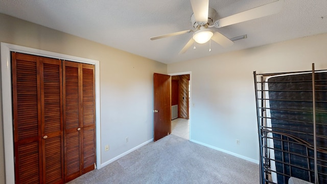 unfurnished bedroom featuring a textured ceiling, ceiling fan, light carpet, and a closet