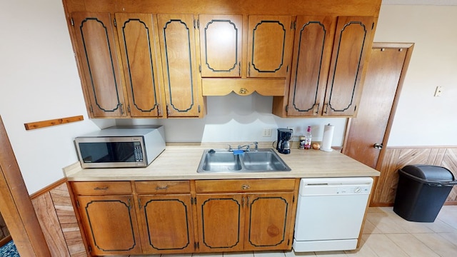 kitchen featuring wood walls, sink, white dishwasher, and light tile patterned floors