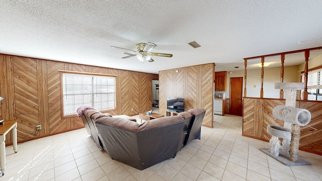 tiled living room featuring a textured ceiling, ceiling fan, and wood walls