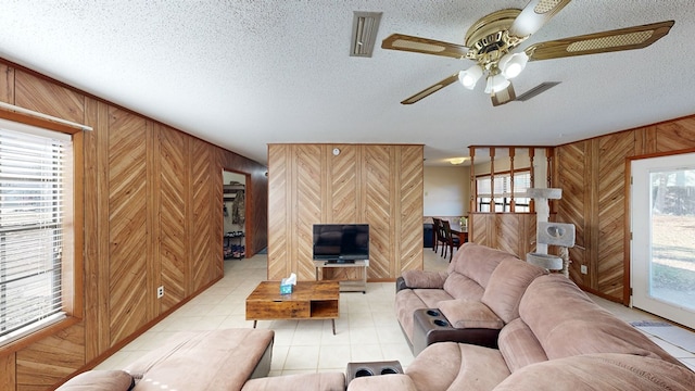 living room featuring a textured ceiling, ceiling fan, a healthy amount of sunlight, and wood walls