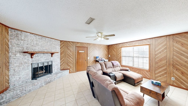 living room featuring ceiling fan, wood walls, a textured ceiling, and a brick fireplace