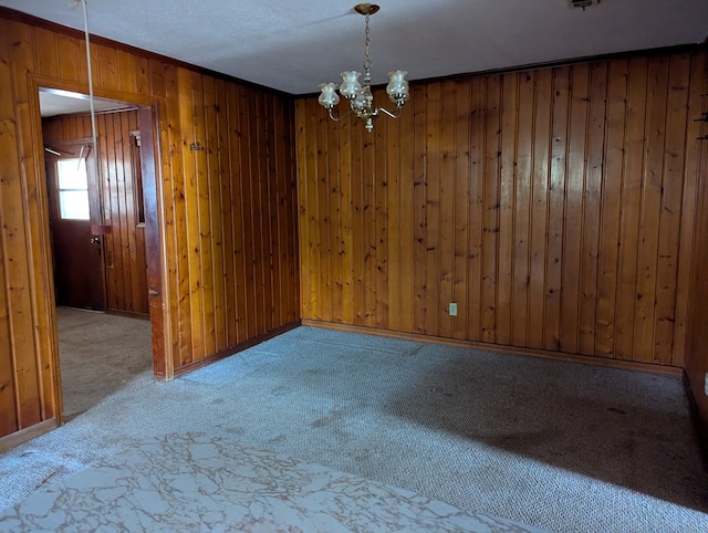 spare room featuring an inviting chandelier, crown molding, wooden walls, and carpet