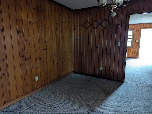 carpeted spare room with wooden walls and a chandelier