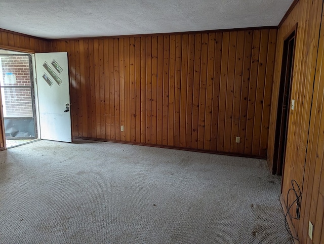 unfurnished room featuring light carpet, crown molding, wooden walls, and a textured ceiling