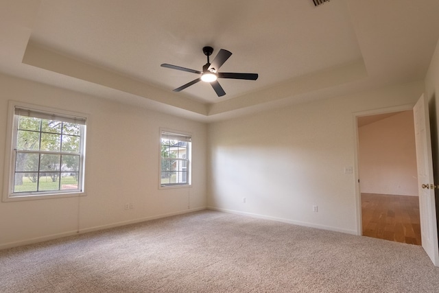 carpeted spare room featuring baseboards, a raised ceiling, and a ceiling fan